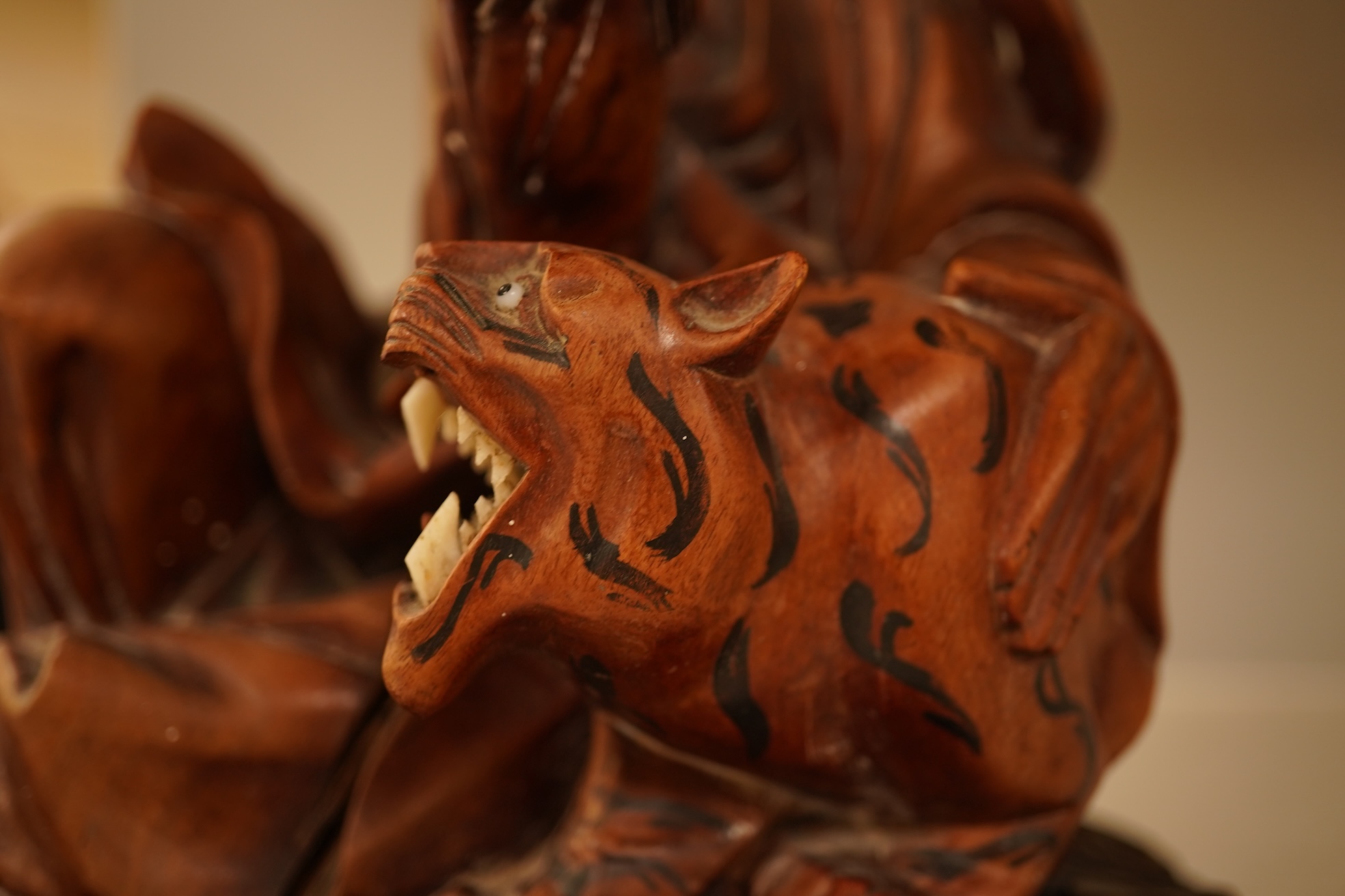 A Chinese hardwood carving of a seated luohan and tiger on hardwood stand, 24cm high including stand.